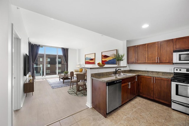 kitchen with sink, a wall of windows, appliances with stainless steel finishes, light tile patterned flooring, and dark stone counters