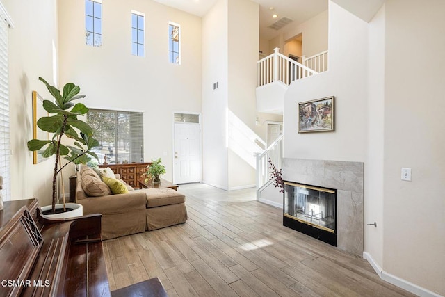 living room featuring a towering ceiling, a fireplace, and light wood-type flooring