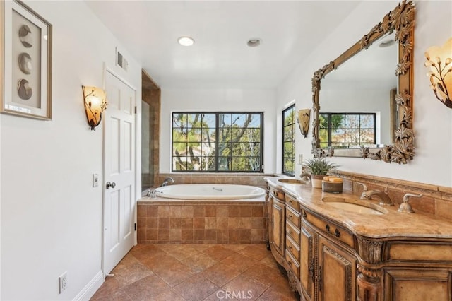 bathroom featuring tiled bath, a wealth of natural light, and vanity