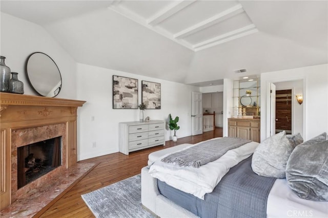 bedroom with a high end fireplace, dark hardwood / wood-style flooring, ensuite bath, and vaulted ceiling