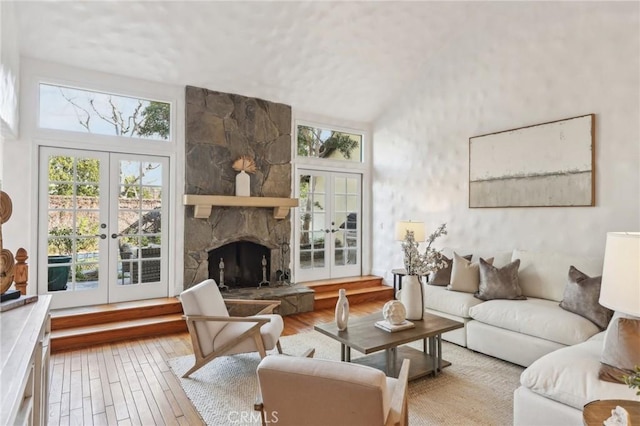 living room with high vaulted ceiling, light hardwood / wood-style flooring, french doors, and a fireplace