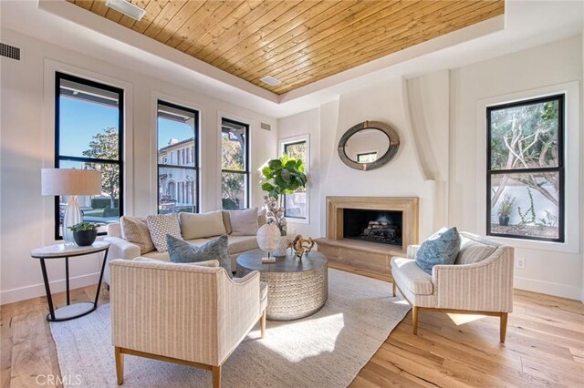 living room featuring a raised ceiling, a healthy amount of sunlight, light hardwood / wood-style floors, and wood ceiling