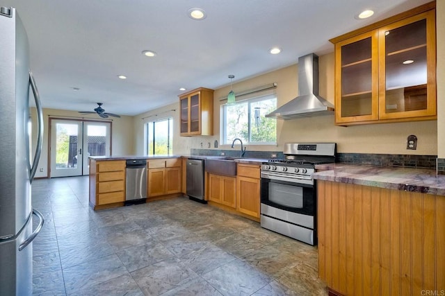 kitchen featuring appliances with stainless steel finishes, decorative light fixtures, ceiling fan, kitchen peninsula, and wall chimney exhaust hood