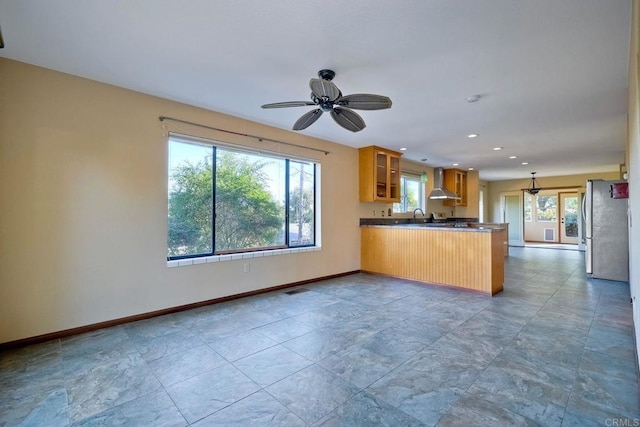 kitchen with wall chimney range hood, stainless steel refrigerator, ceiling fan, decorative light fixtures, and kitchen peninsula