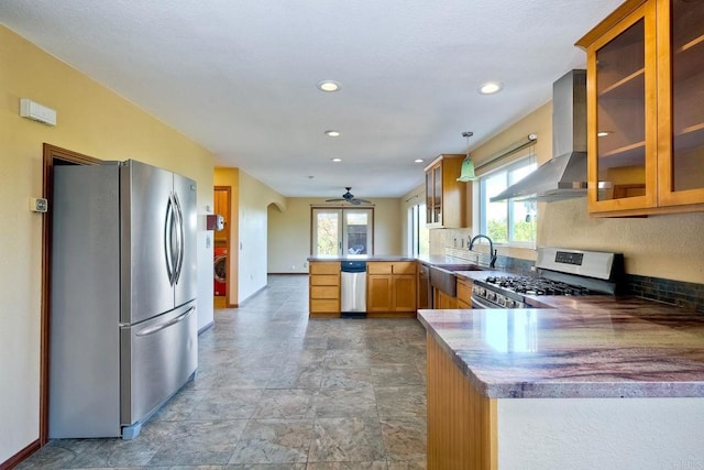 kitchen featuring wall chimney exhaust hood, ceiling fan, stainless steel appliances, and kitchen peninsula