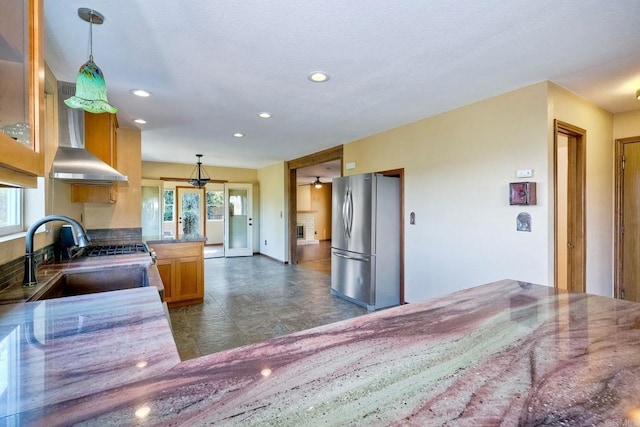 kitchen with hanging light fixtures, sink, stainless steel fridge, and wall chimney exhaust hood