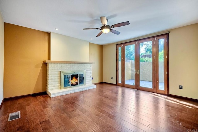 unfurnished living room featuring wood-type flooring, a brick fireplace, ceiling fan, and french doors