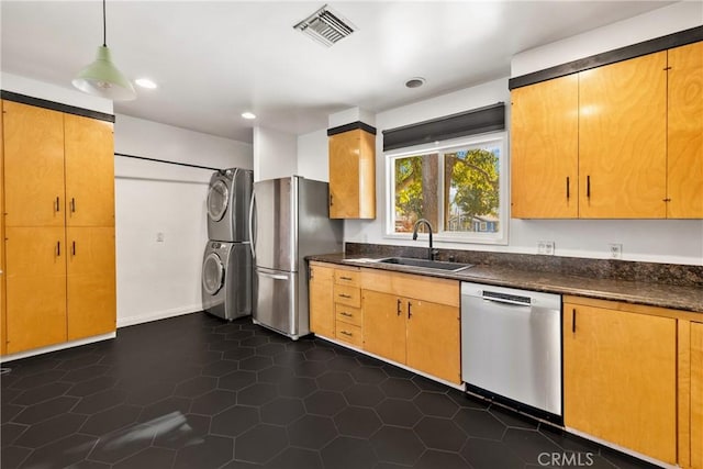 kitchen featuring stacked washer and dryer, stainless steel appliances, decorative light fixtures, dark tile patterned flooring, and sink