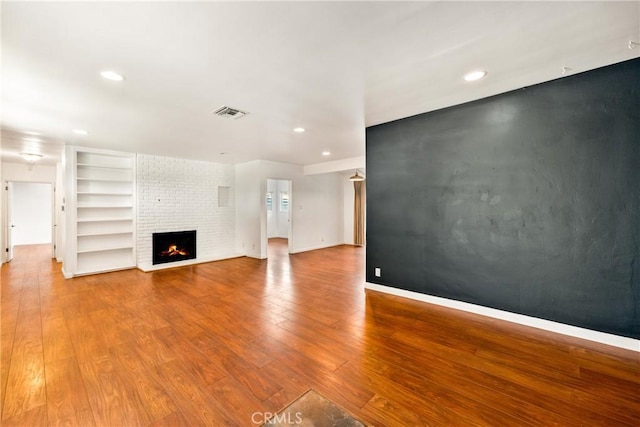 unfurnished living room with a brick fireplace, hardwood / wood-style flooring, and built in features