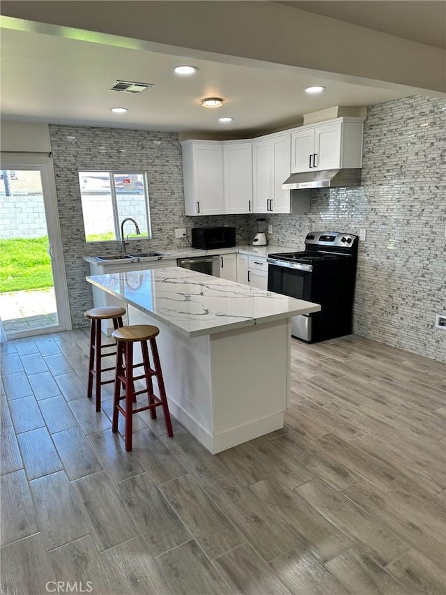 kitchen with electric stove, a kitchen island, backsplash, white cabinetry, and sink