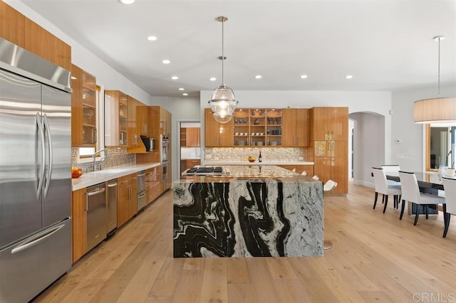 kitchen featuring pendant lighting, appliances with stainless steel finishes, a center island, and light stone counters