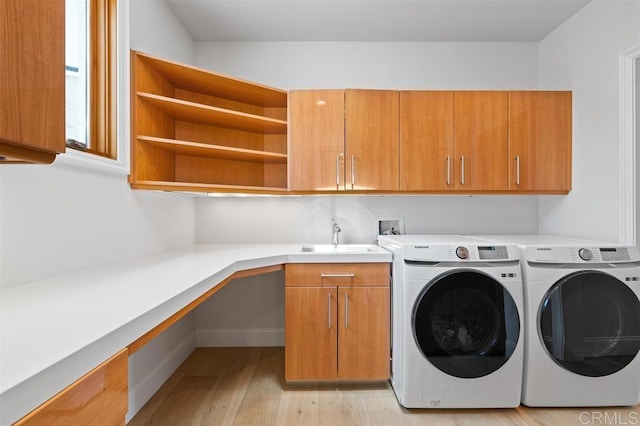 laundry area featuring cabinets, washer and dryer, sink, and light wood-type flooring