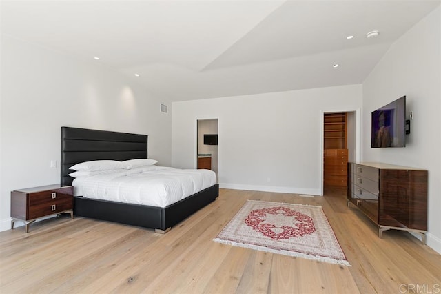 bedroom with vaulted ceiling, a walk in closet, light wood-type flooring, and a closet