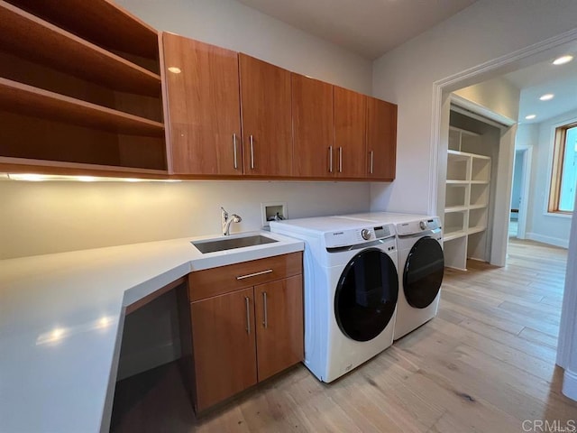 laundry room with cabinets, light hardwood / wood-style floors, sink, and washing machine and clothes dryer