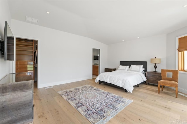 bedroom featuring a walk in closet, vaulted ceiling, light wood-type flooring, baseboards, and visible vents