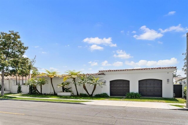 mediterranean / spanish home with a tiled roof, stucco siding, fence, and an attached garage