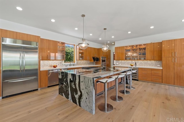 kitchen featuring light wood-style floors, stainless steel appliances, brown cabinetry, and glass insert cabinets