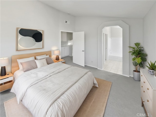 bedroom featuring light carpet, lofted ceiling, and connected bathroom