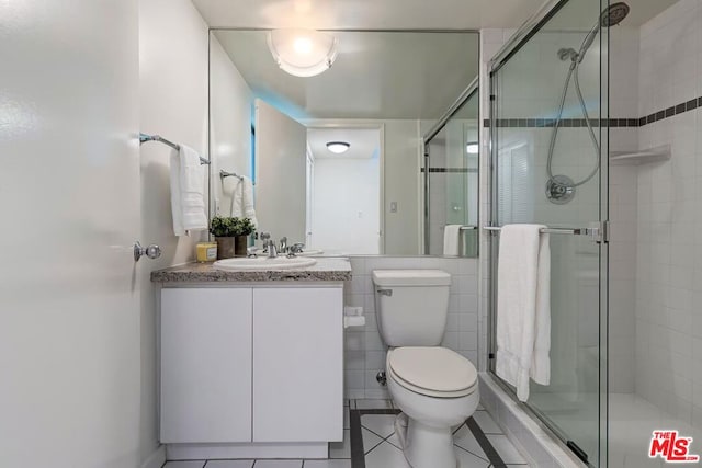 bathroom with toilet, tile walls, tile patterned floors, a shower with shower door, and vanity