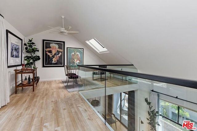 hallway with lofted ceiling with skylight and light wood-type flooring