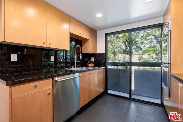 kitchen with sink, tasteful backsplash, stainless steel dishwasher, dark stone counters, and dark tile patterned floors