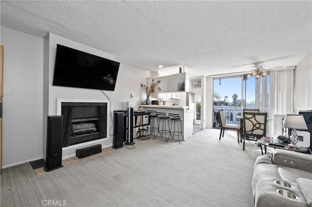 living room featuring ceiling fan, expansive windows, light carpet, and a textured ceiling