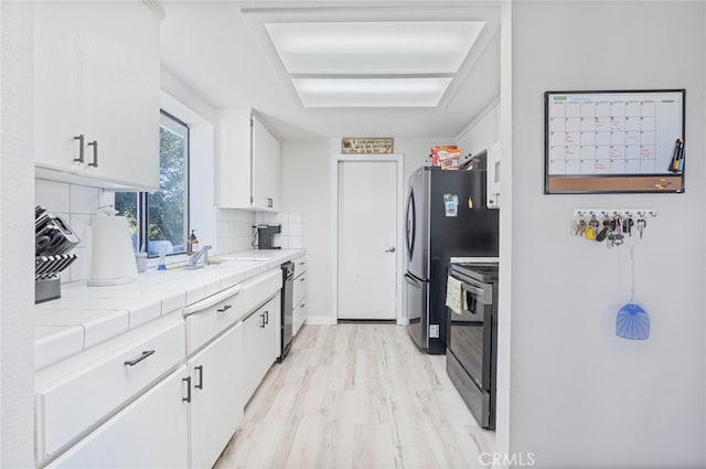 kitchen featuring stainless steel appliances, light wood-type flooring, tile countertops, decorative backsplash, and white cabinets