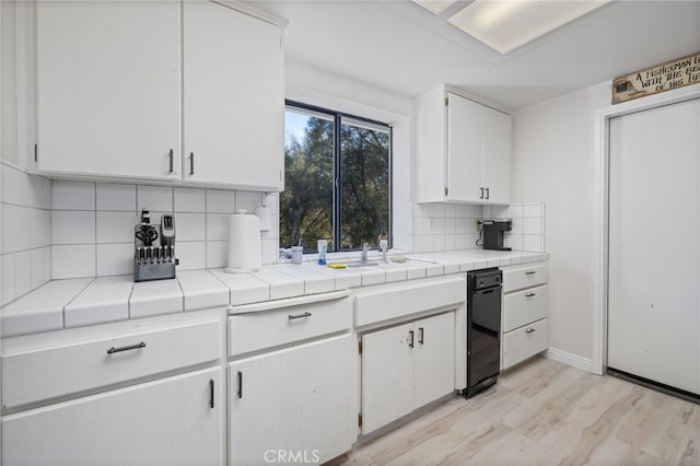 kitchen featuring tile countertops, decorative backsplash, light wood-type flooring, white cabinetry, and sink