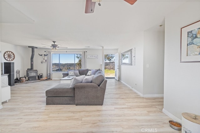 living room with light hardwood / wood-style floors, ceiling fan, and a wood stove