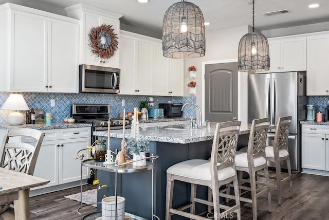 kitchen featuring a breakfast bar area, a center island with sink, appliances with stainless steel finishes, pendant lighting, and white cabinetry