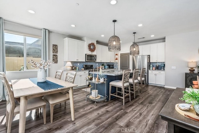 kitchen featuring light stone countertops, hanging light fixtures, a kitchen island with sink, white cabinets, and appliances with stainless steel finishes