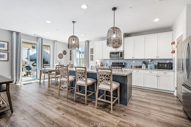 kitchen featuring light stone counters, pendant lighting, a kitchen island with sink, white cabinets, and appliances with stainless steel finishes