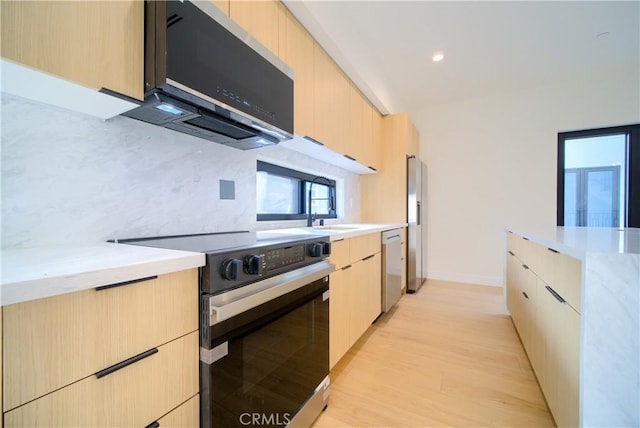 kitchen featuring sink, appliances with stainless steel finishes, tasteful backsplash, light brown cabinets, and light wood-type flooring