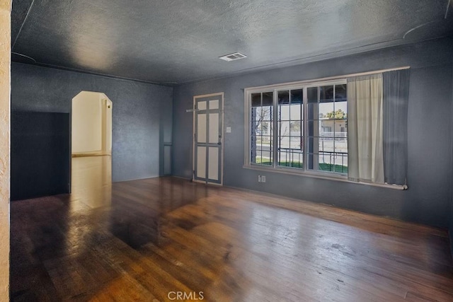 empty room with arched walkways, visible vents, a textured ceiling, and wood finished floors