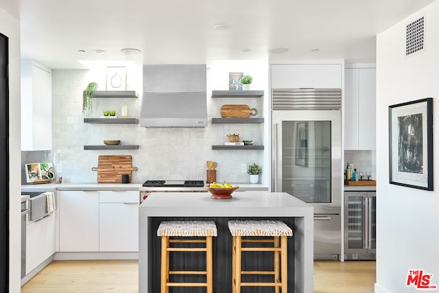 kitchen with white cabinetry, wall chimney exhaust hood, a breakfast bar area, backsplash, and wine cooler