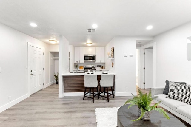 kitchen with white cabinets, appliances with stainless steel finishes, a kitchen bar, sink, and kitchen peninsula