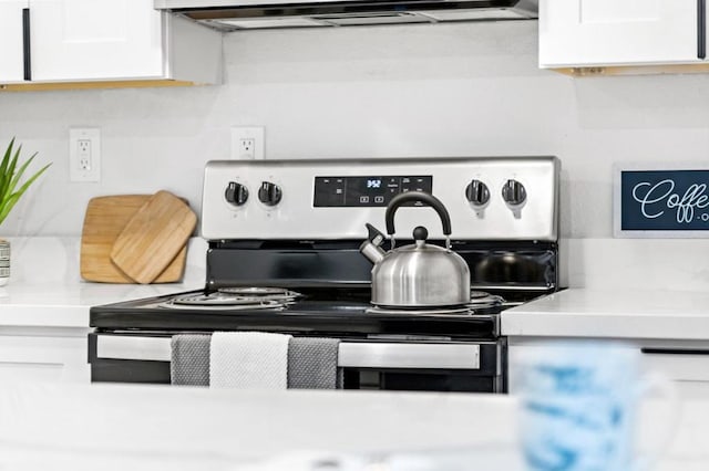 interior details with electric stove, white cabinetry, and ventilation hood