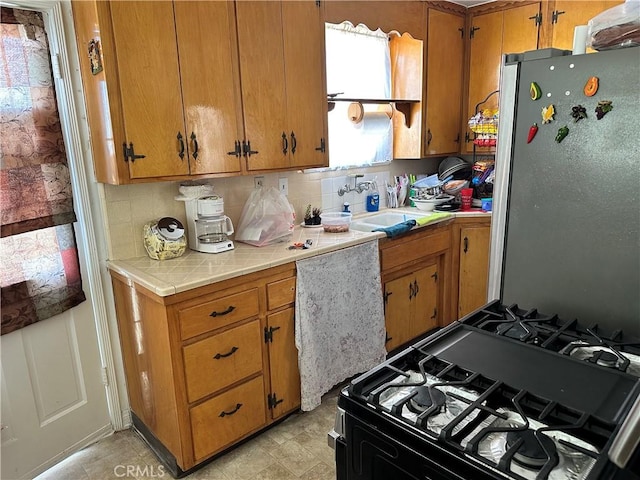 kitchen featuring tasteful backsplash, sink, stainless steel refrigerator, and gas range