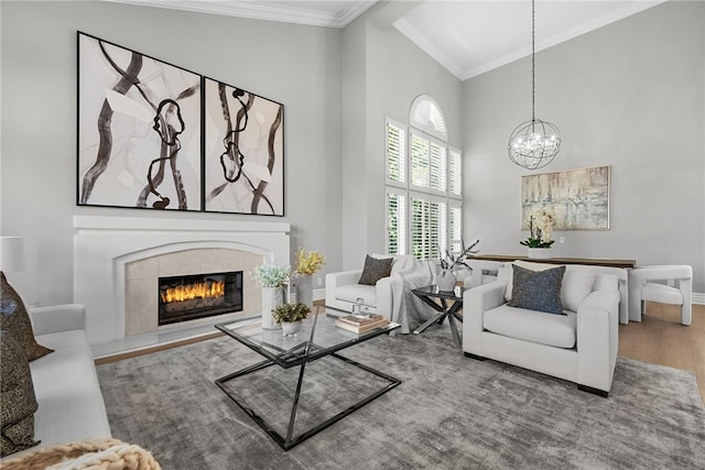 living room with a tile fireplace, wood-type flooring, an inviting chandelier, crown molding, and high vaulted ceiling