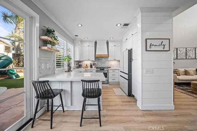 kitchen featuring kitchen peninsula, custom range hood, a kitchen bar, stainless steel gas stove, and white cabinets