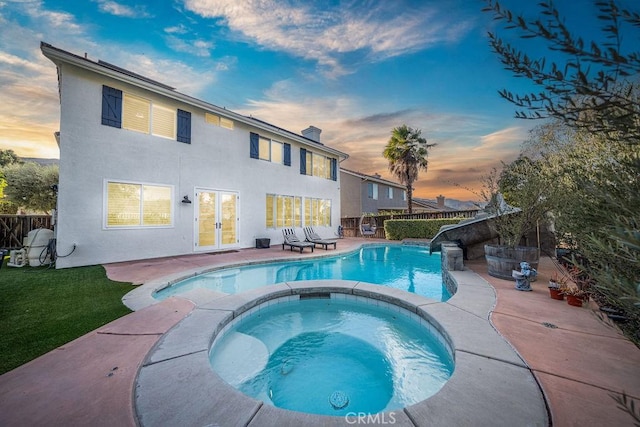 pool at dusk with an in ground hot tub and a patio area