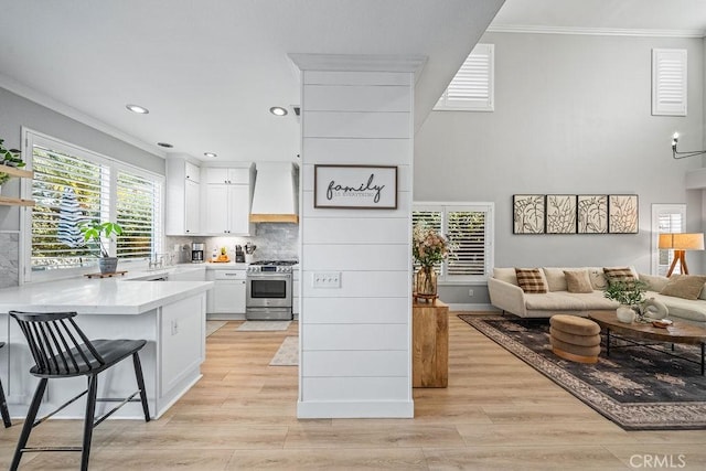 kitchen featuring a kitchen breakfast bar, custom exhaust hood, stainless steel gas range oven, ornamental molding, and white cabinetry