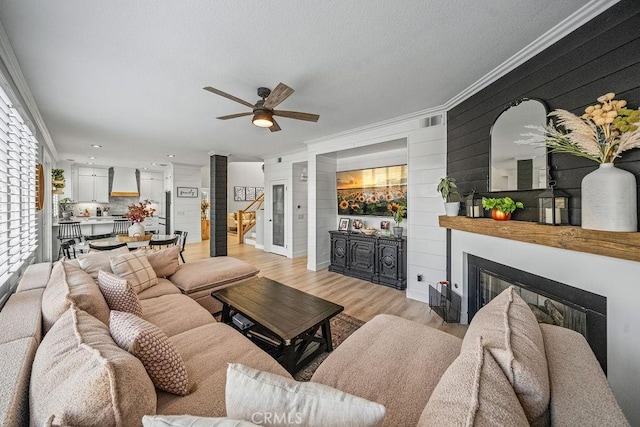 living room with light hardwood / wood-style floors, ceiling fan, crown molding, and a textured ceiling