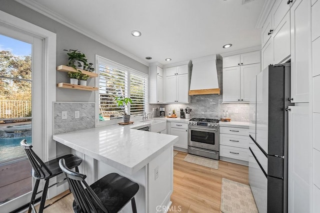 kitchen with kitchen peninsula, custom exhaust hood, stainless steel gas stove, white cabinets, and ornamental molding