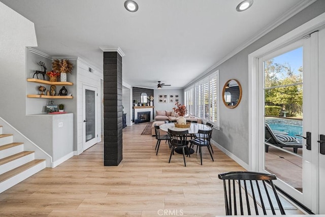 dining space with light hardwood / wood-style floors, ornamental molding, ceiling fan, and a large fireplace