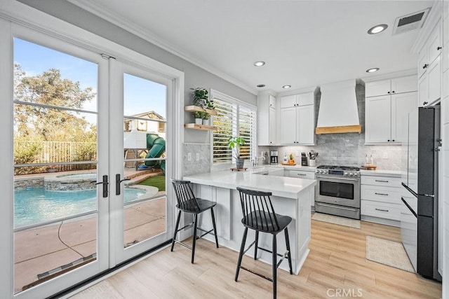 kitchen with white cabinets, high end stainless steel range oven, french doors, kitchen peninsula, and custom exhaust hood