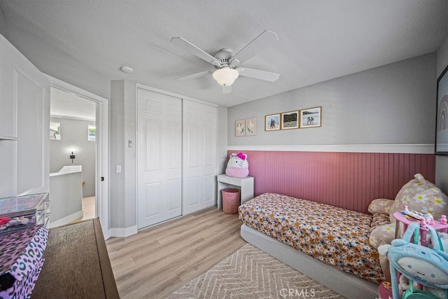 bedroom featuring ceiling fan, light wood-type flooring, a closet, and a textured ceiling