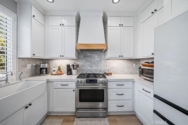 kitchen with appliances with stainless steel finishes, backsplash, custom range hood, and white cabinetry