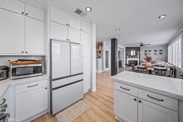 kitchen featuring a large fireplace, white fridge, light wood-type flooring, white cabinetry, and ceiling fan