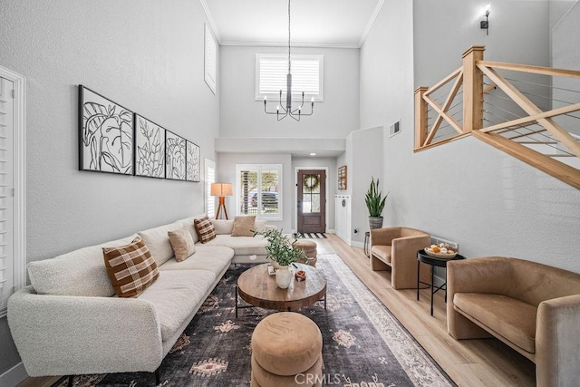 living room with a towering ceiling, a notable chandelier, crown molding, and light hardwood / wood-style flooring